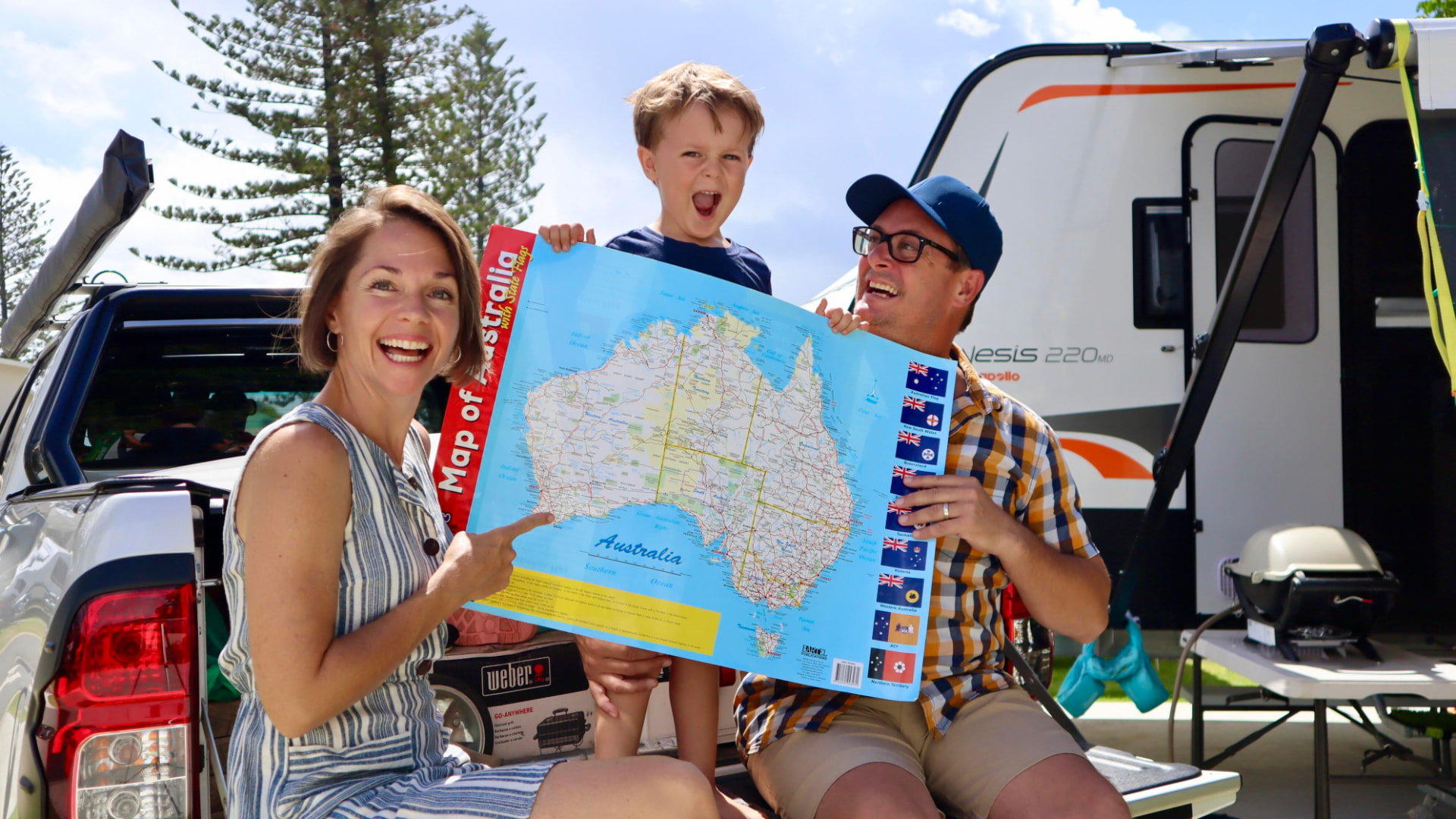 The family beside their caravan holding a map of Australia