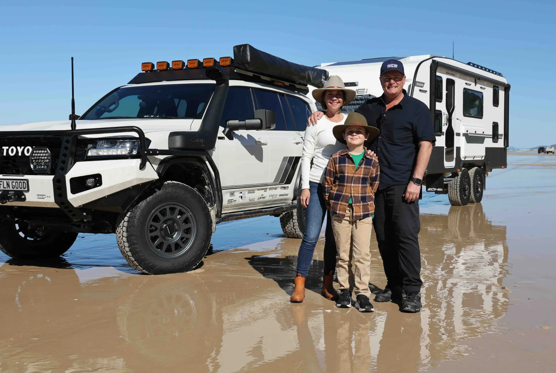Katie, Paul and Jasper together beside their touring vehicle and caravan on the beach