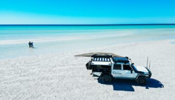 Beautiful blue water beach with 4x4 vehicle and family enjoying the water