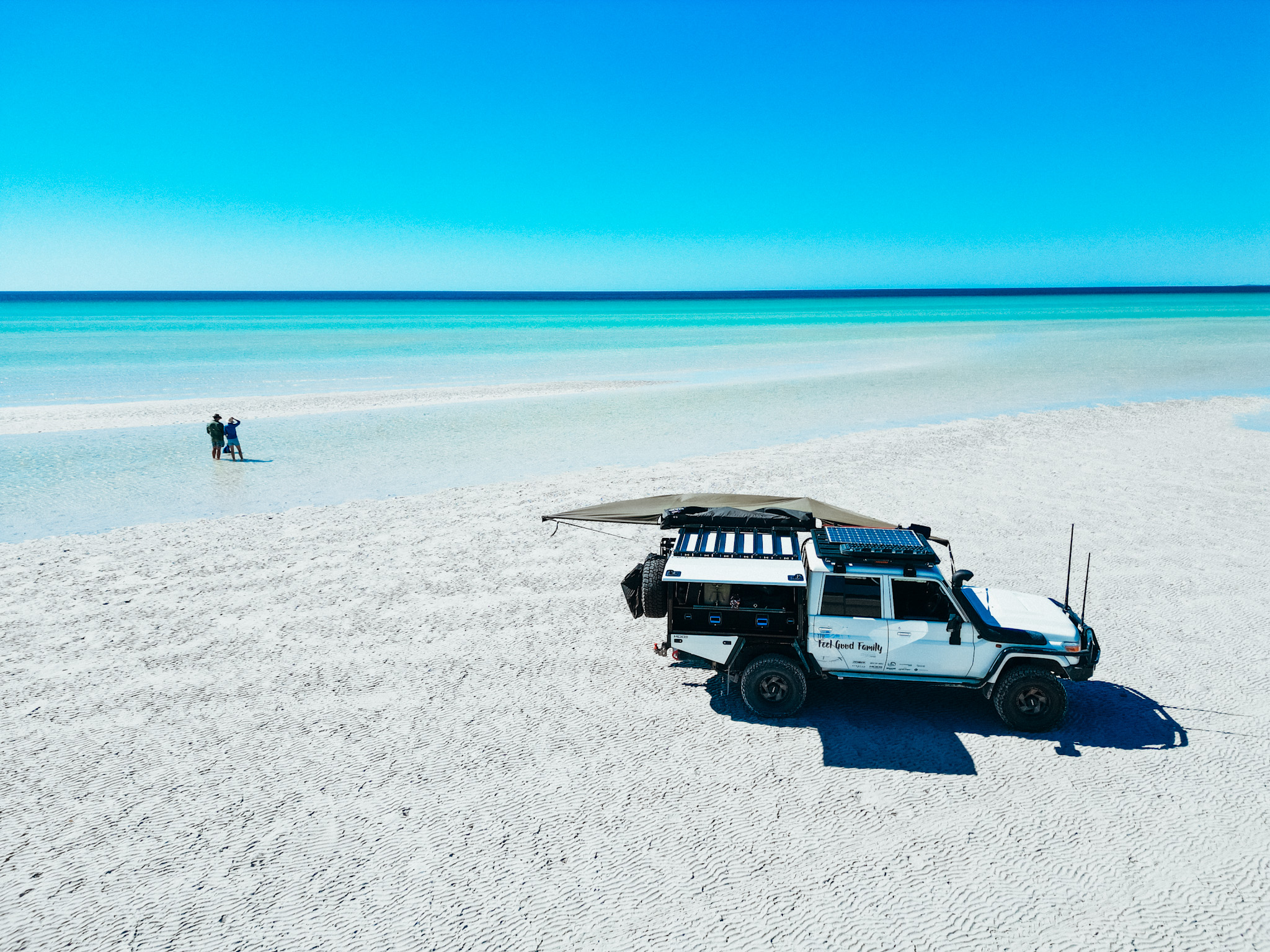 Beautiful blue water beach with 4x4 vehicle and family enjoying the water